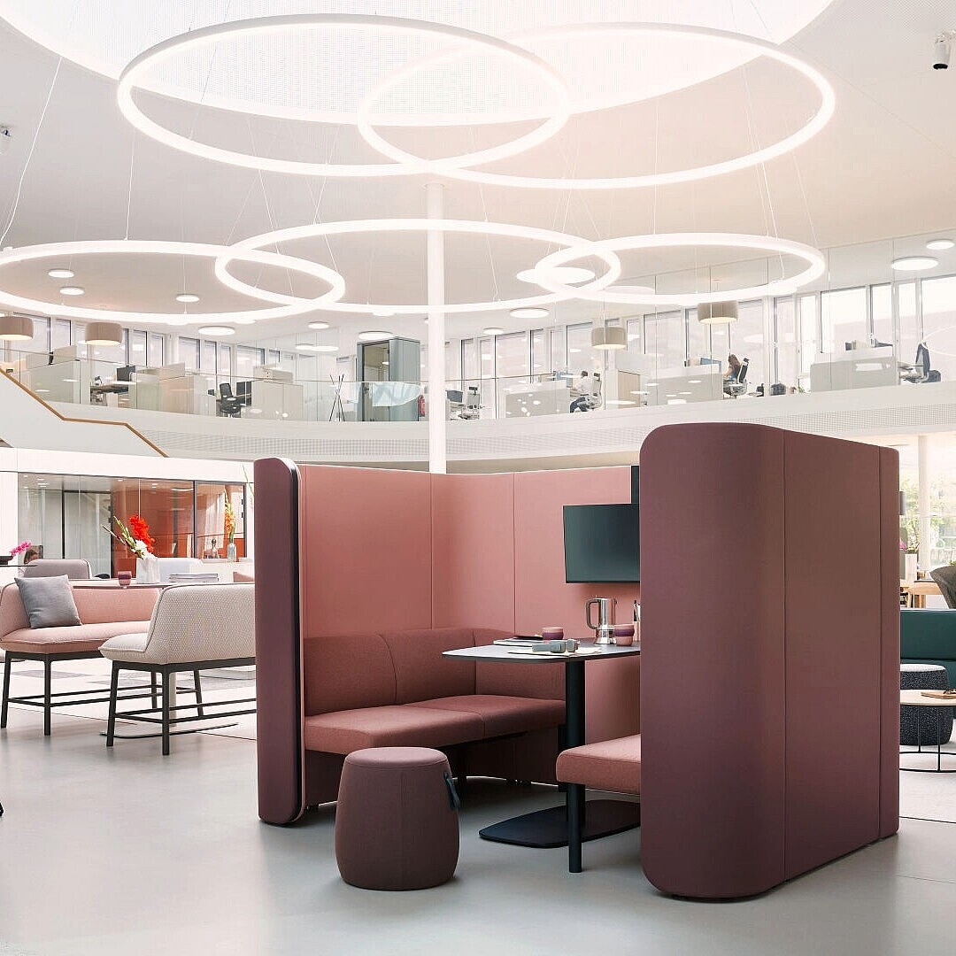 Open office space with se:hive room solution featuring a curved high-backed booth with table and stools, surrounded by various seating areas and circular ceiling lights