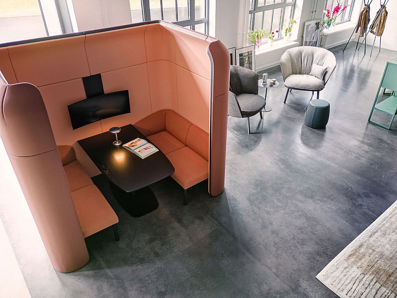 Modulable se:hive avec des parois hautes et un banc intégré autour d’une table noire, à côté de deux fauteuils et d’une petite table ronde dans un espace de bureau lumineux avec de grandes fenêtres.