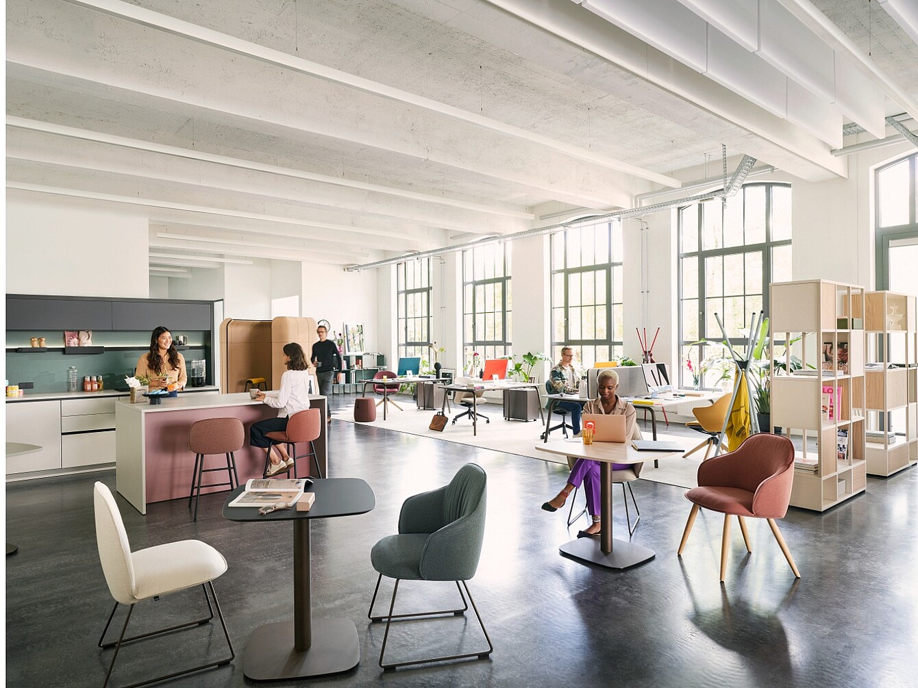 Large open room with tall windows, multiple tables and chairs, and people working at computers