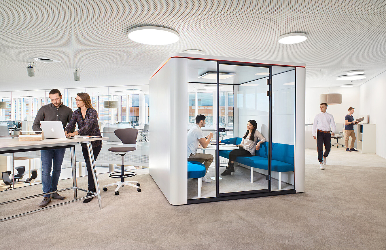 Modern office with an enclosed meeting pod and employees working in open and private areas.