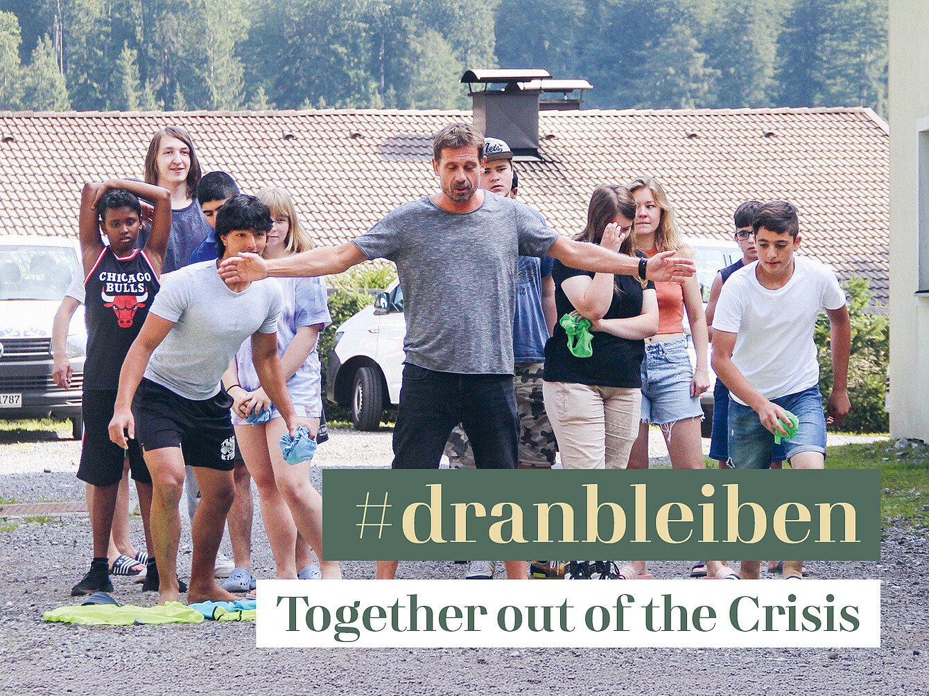 Groupe de jeunes à l’extérieur, certains faisant des étirements et d’autres debout, avec un bâtiment et des voitures garées en arrière-plan, surmonté du texte « #dranbleiben Ensemble pour sortir de la crise ».