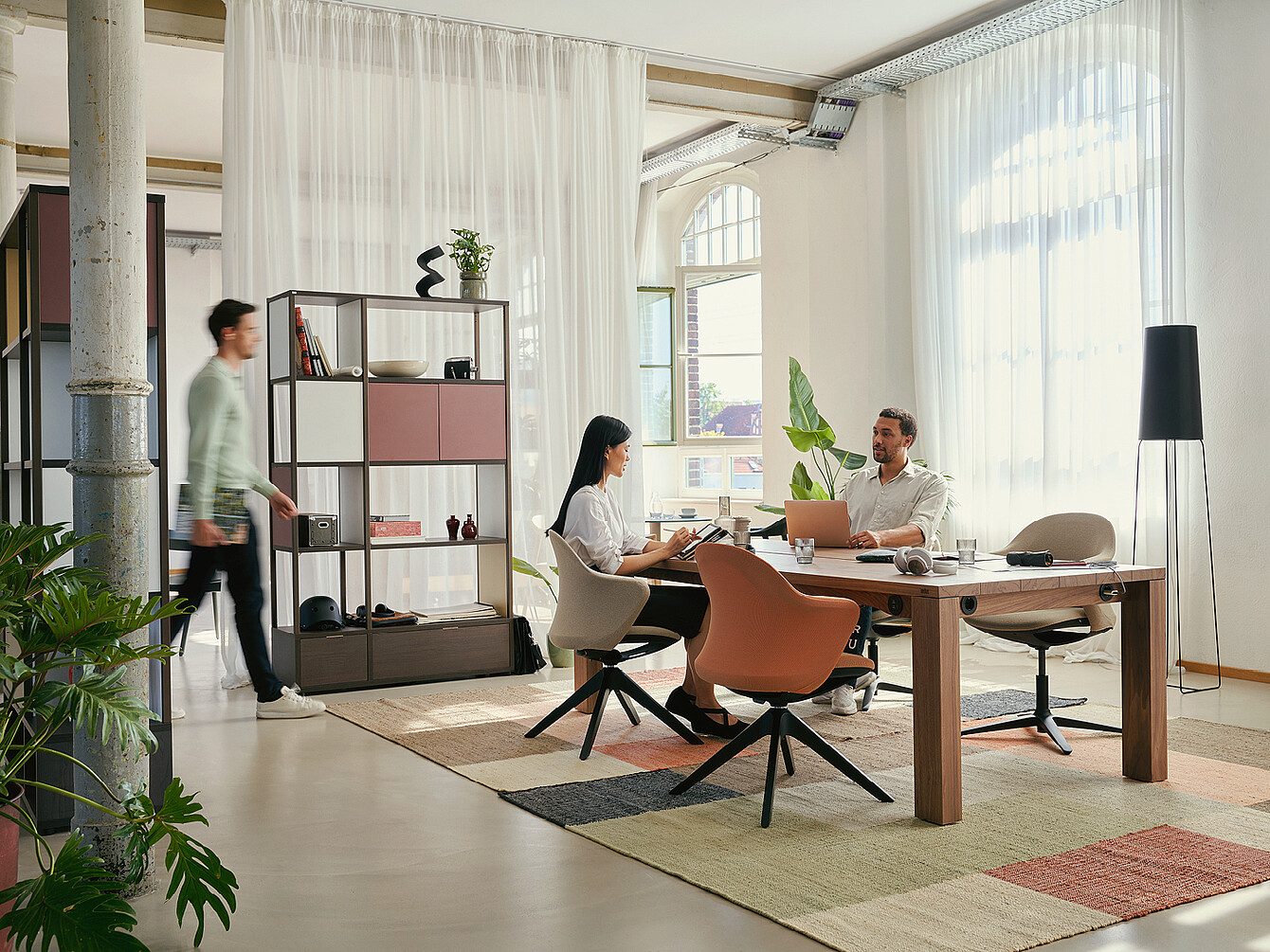 Moderne hybride duktile Gemeinfläche mit zwei Personen im Gespräch an einem Holztisch, flexiblen Stühlen und viel Tageslicht in einem offenen, hellen Büro