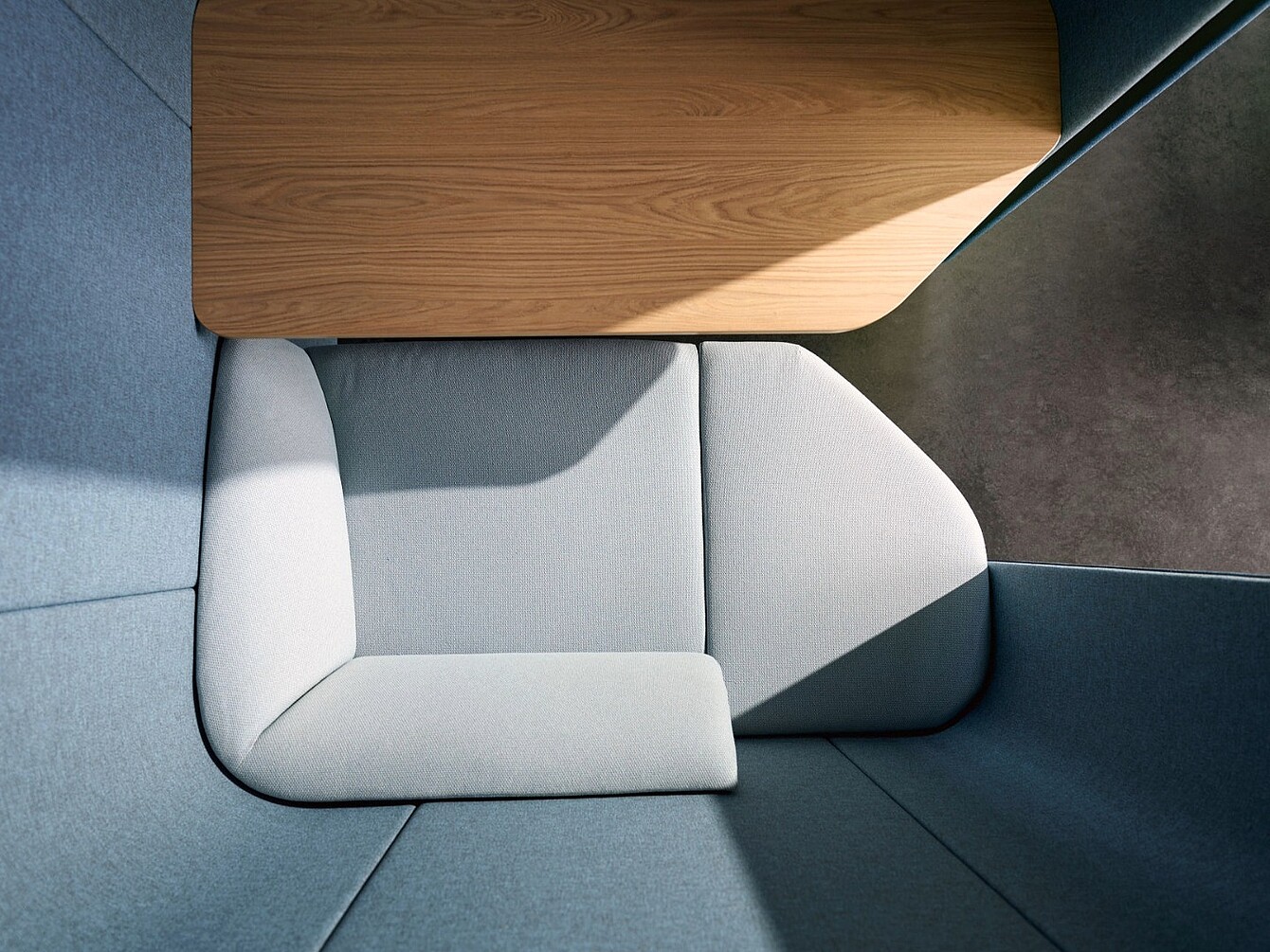 Vue de dessus d’un ensemble de sièges modulaires avec des coussins gris clair et une surface de table en bois dans un coin.