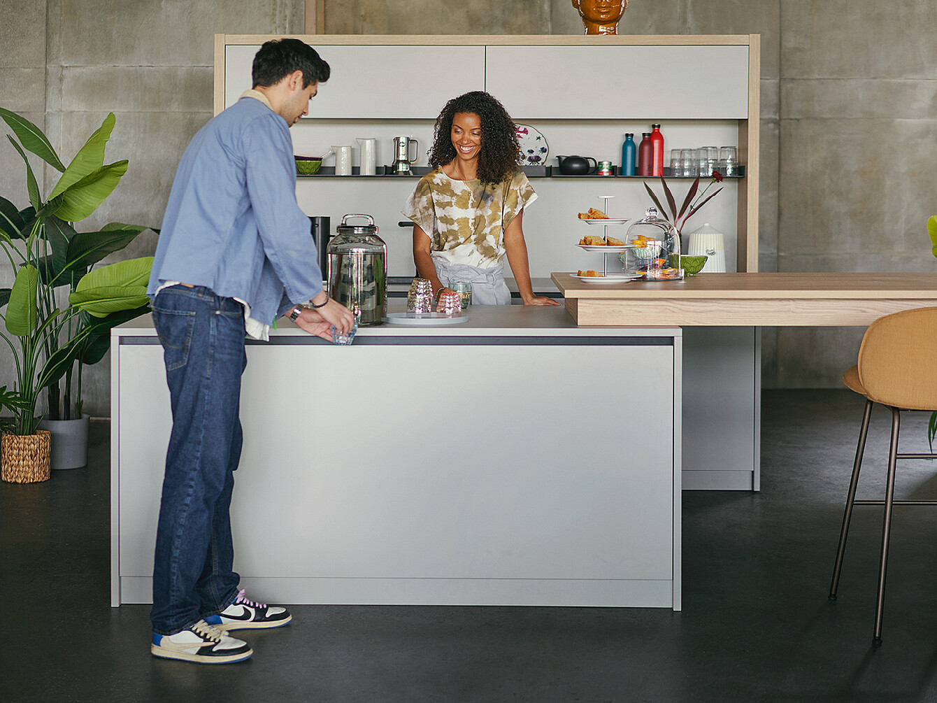 Zwei Personen in einer modernen, hybriden duktile Gemeinfläche mit Kücheninsel, Pflanzen und Snacks, die Gemeinschaft und Flexibilität am Arbeitsplatz fördern