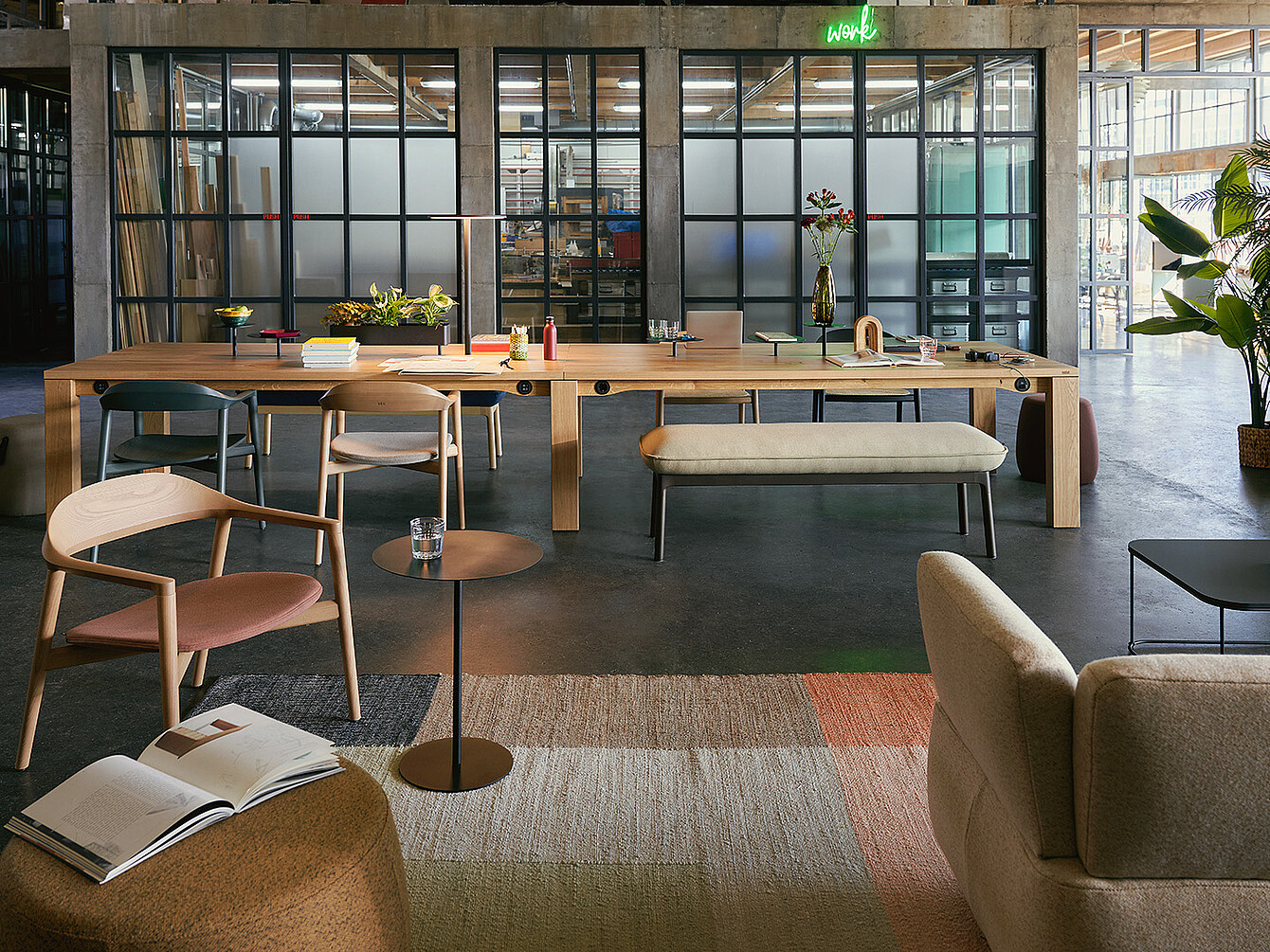 Moderne kantoorlounge met houten stoelen, een lange houten tafel met boeken en bloemen en een glazen wand met zwarte lijsten