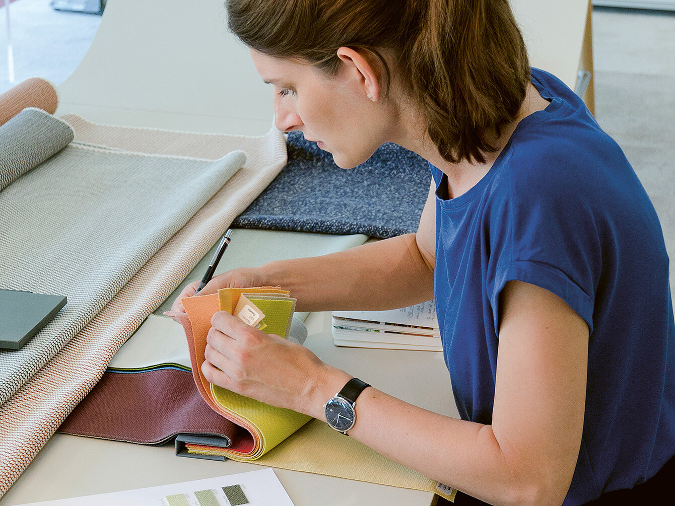 Industrieel ontwerper Judith Daur bekijkt stofstalen, gericht op kleur en textuur, in een werkruimte gevuld met verschillende materialen.
