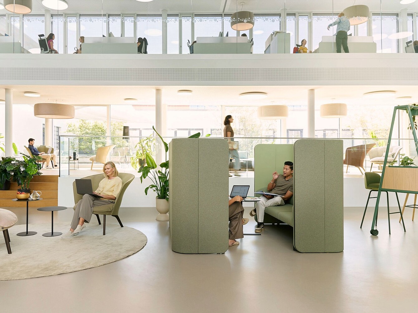 Espace de bureau ouvert avec se:hive modulaire créant des zones de repli semi-fermées, entourées de sièges, de tables, de plantes et de personnes qui travaillent ou marchent.