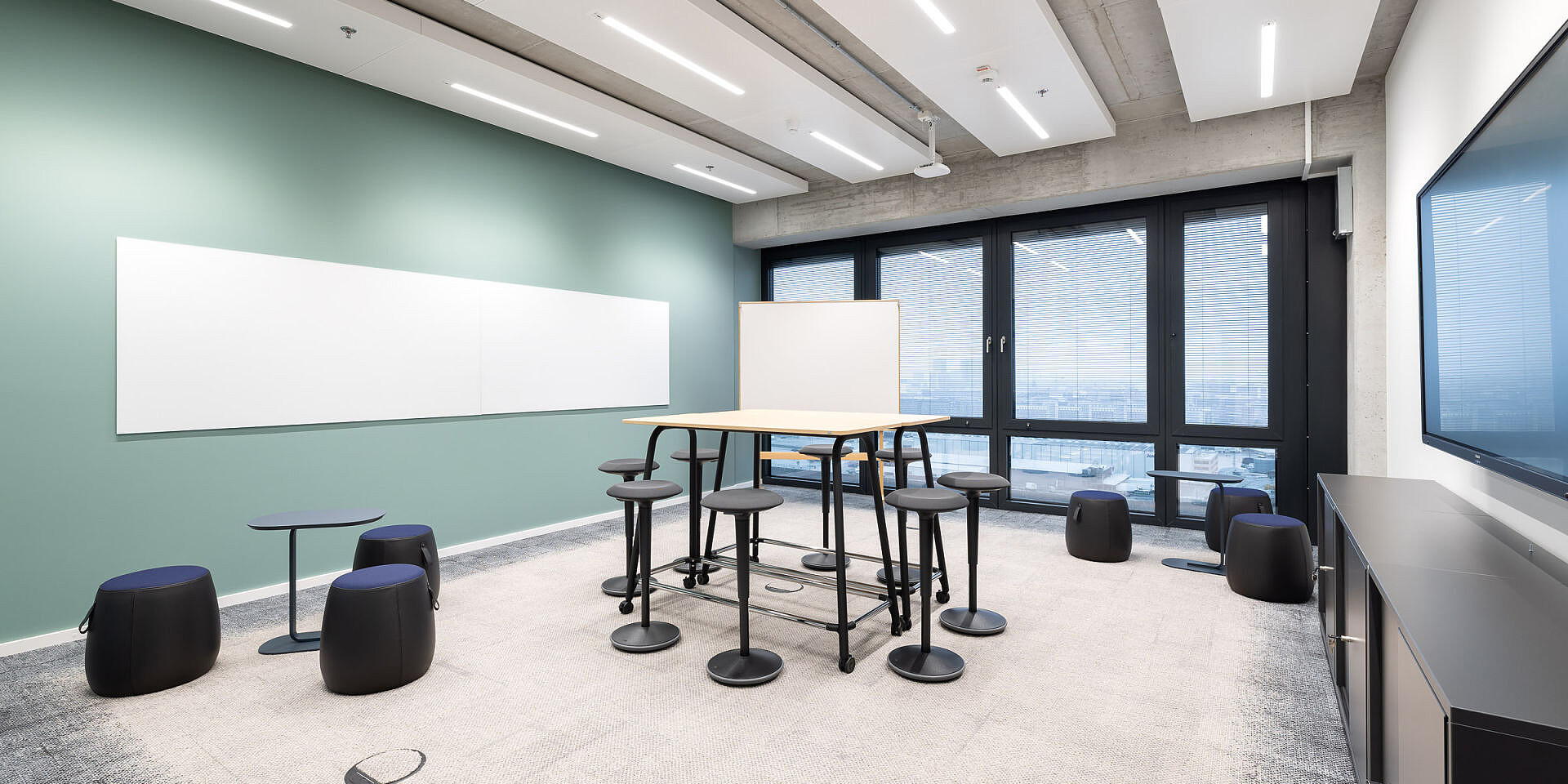 Moderna sala de reuniones con mesa de taller se:lab high desk, asientos de pie se:fit y taburetes se:dot para un trabajo ágil y la colaboración. 