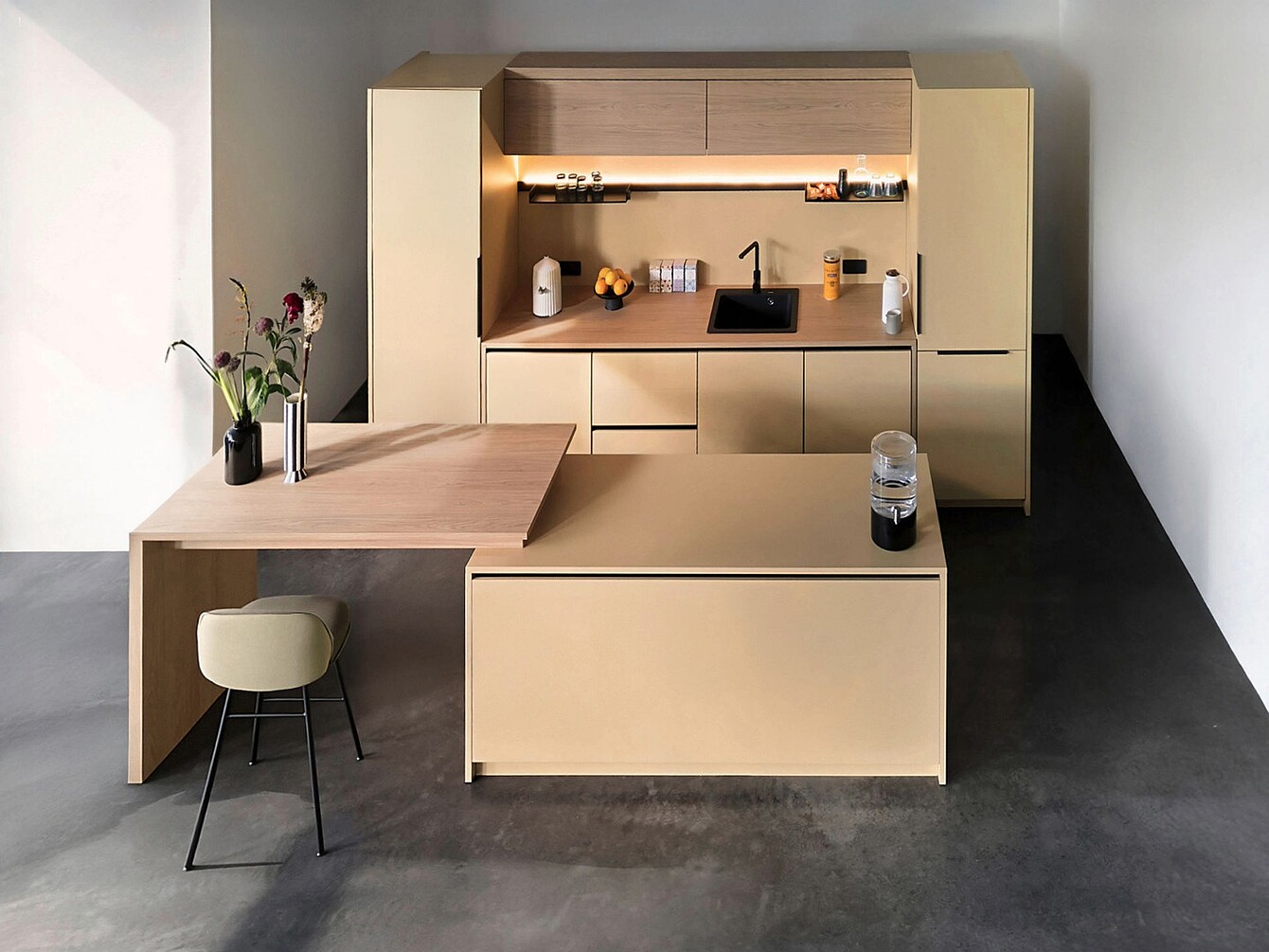 Aménagement minimaliste du se:café bar avec des armoires hautes beiges, un évier intégré, un éclairage sous les armoires, une extension de plan de travail en bois avec un tabouret, et des vases décoratifs avec des fleurs