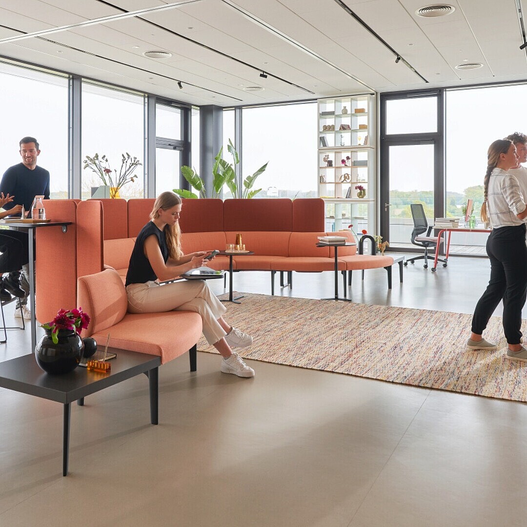 Several people in a modern open office with seating areas, large windows, and a whiteboard where two people are standing