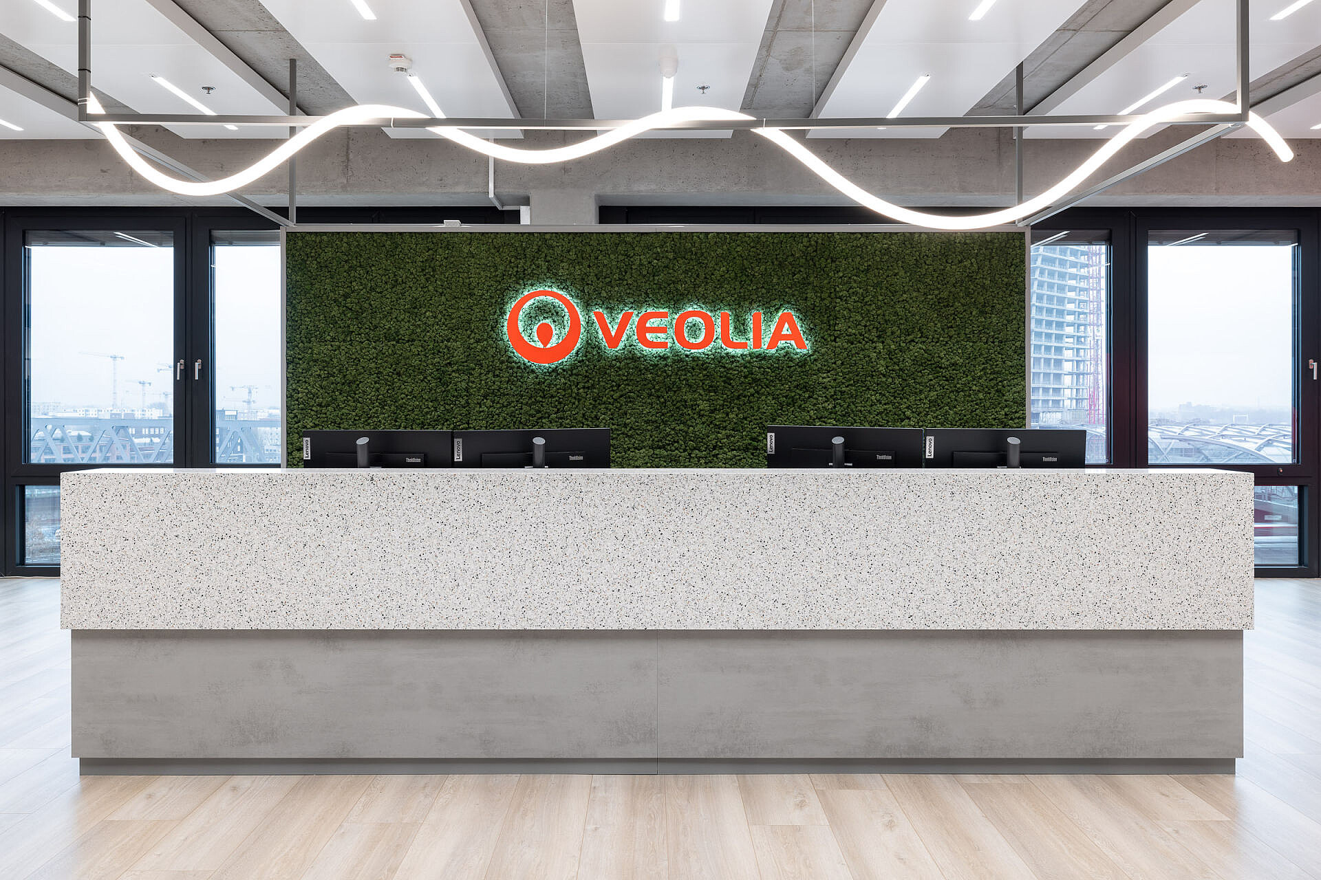 Imagen de portada de la página de referencia de Veolia Hamburg en el sitio web de Sedus: mostrador de recepción en una oficina moderna con fondo verde y el logotipo de Veolia en naranja y blanco. 