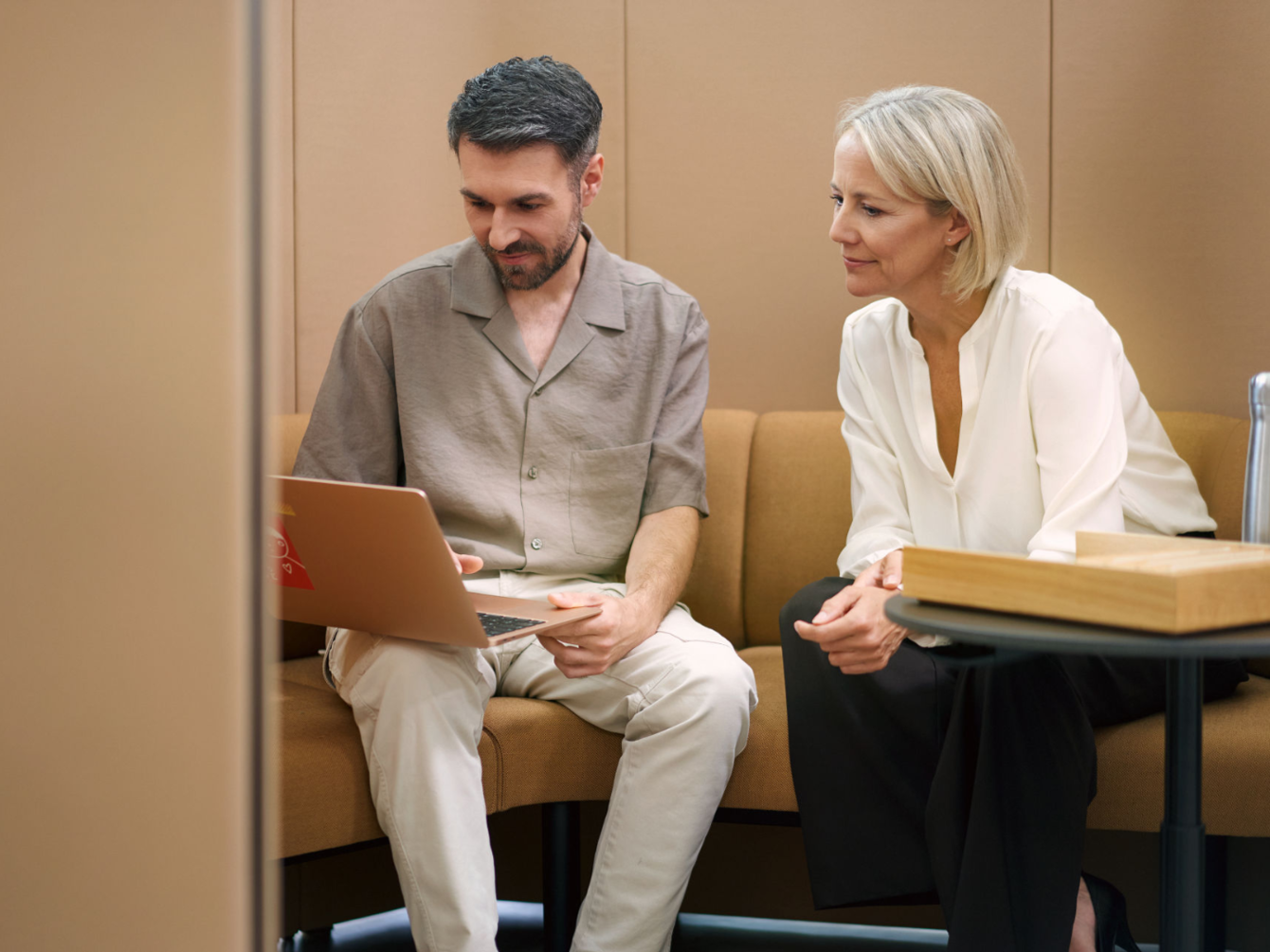 Dos personas están sentadas juntas en una cabina de asiento aislada y observan un ordenador portátil.