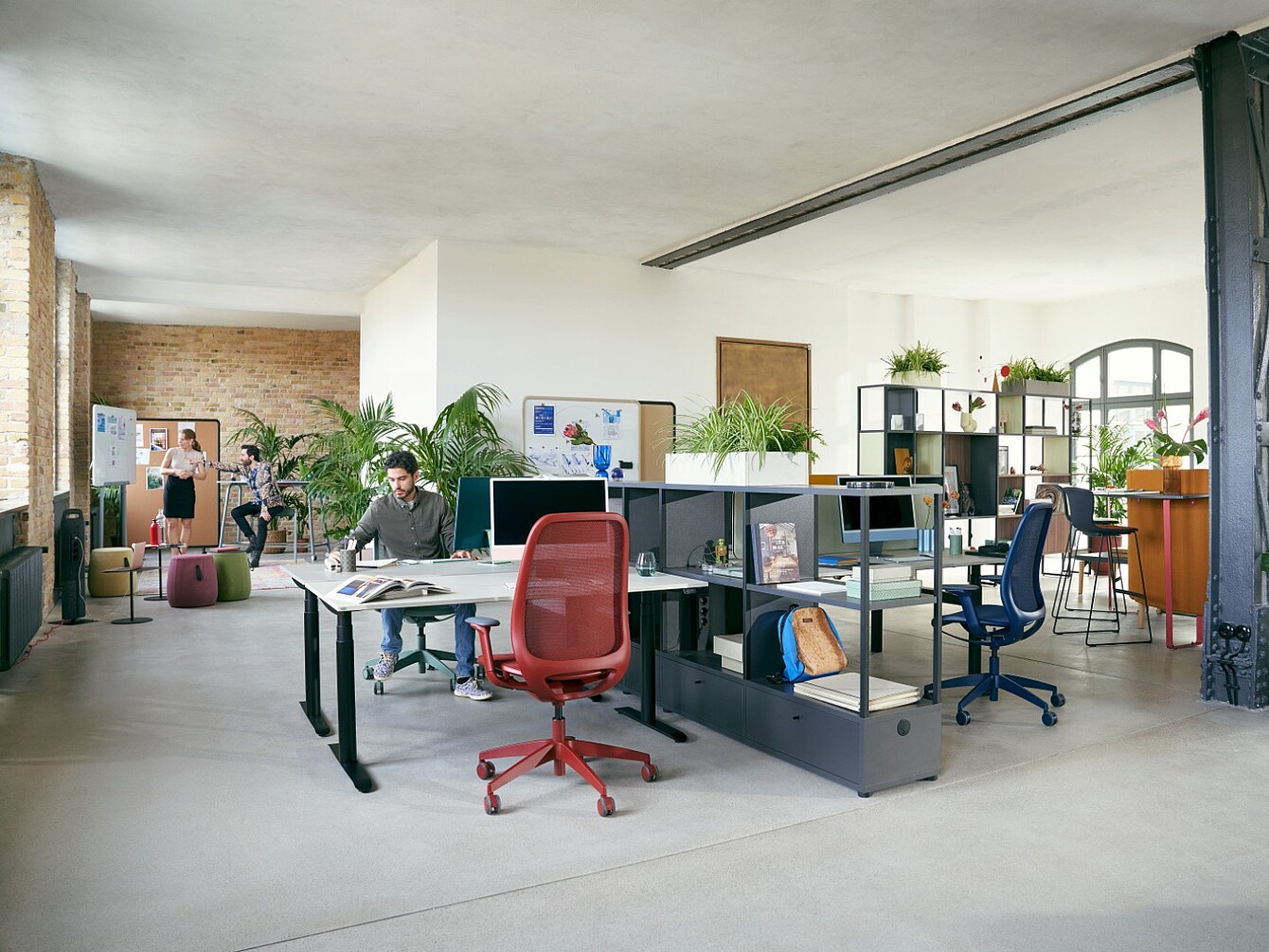 Bureau en open space avec des bureaux séparés par des étagères basses, des personnes au travail et des plantes sur les étagères et les bureaux